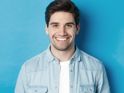 close-up-young-successful-man-smiling-camera-standing-casual-outfit-against-blue-background